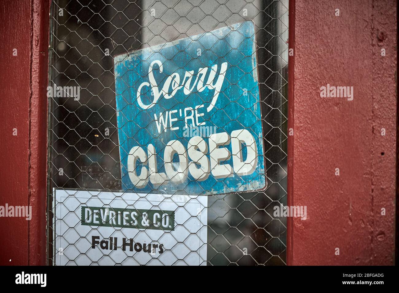 Green Sorry we're closed sign on red door safety wire in glass Stock Photo