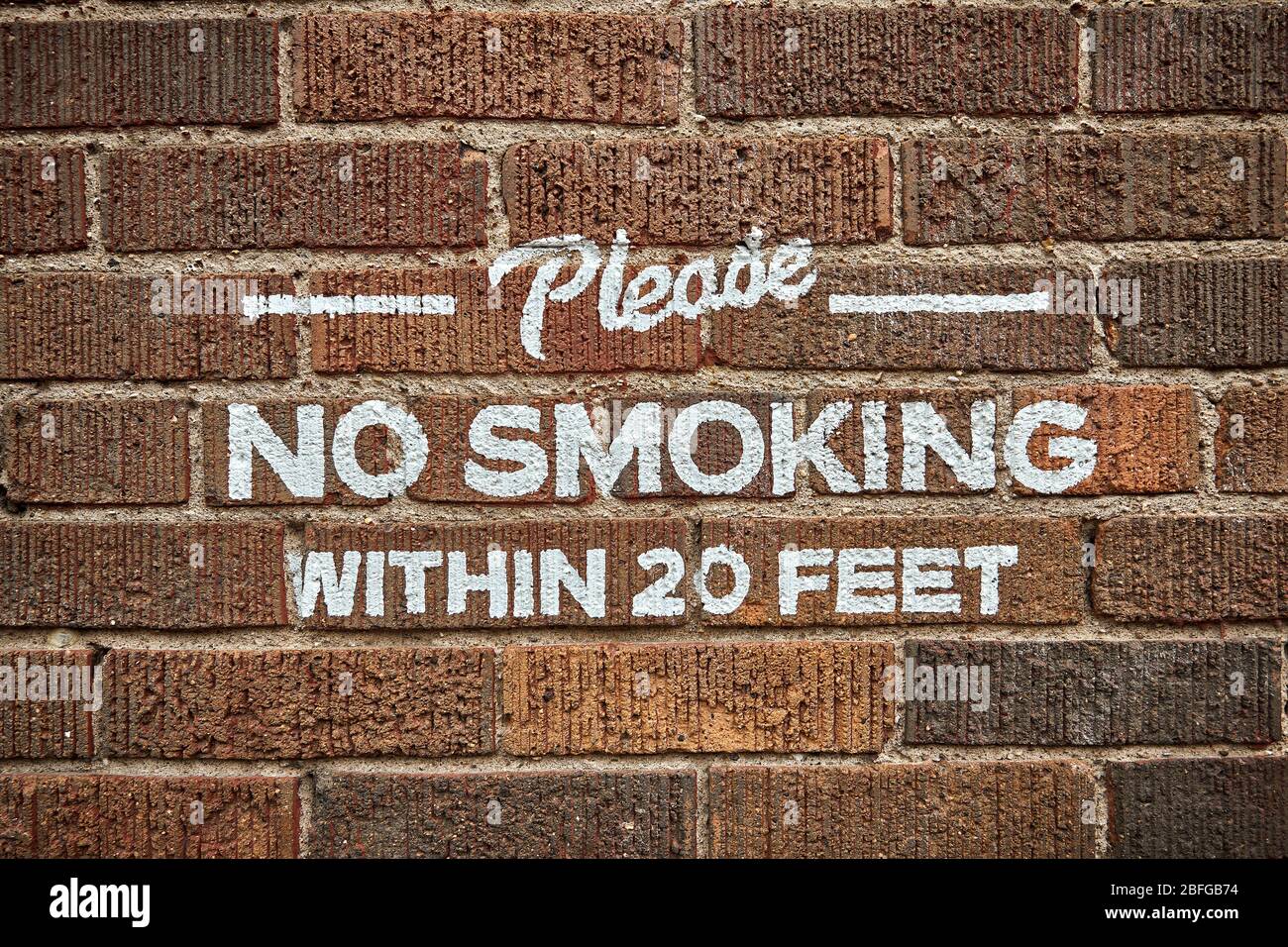 Please No Smoking within 20 feet painted in white on a red brick wall Stock Photo