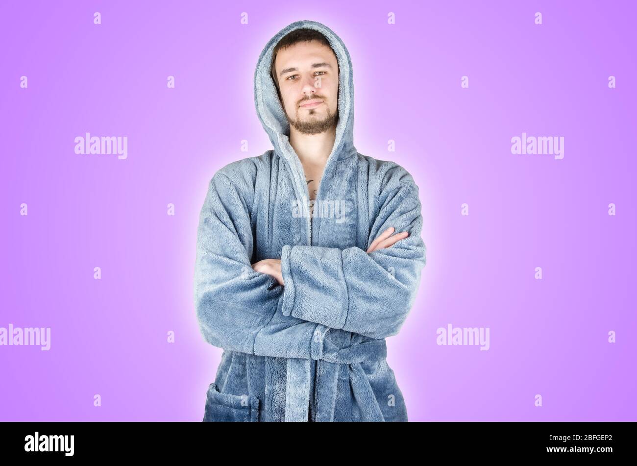 Portrait of young caucasian bearded man in blue bathrobe with crossed hands isolated on purple background. Confident emotion concept Stock Photo