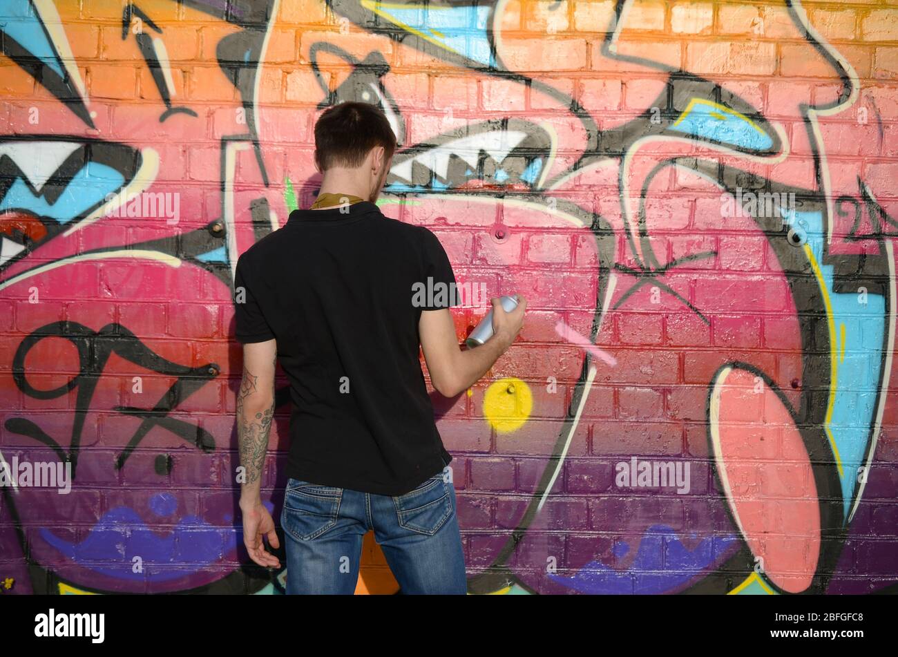 Young graffiti artist with backpack and gas mask on his neck paints