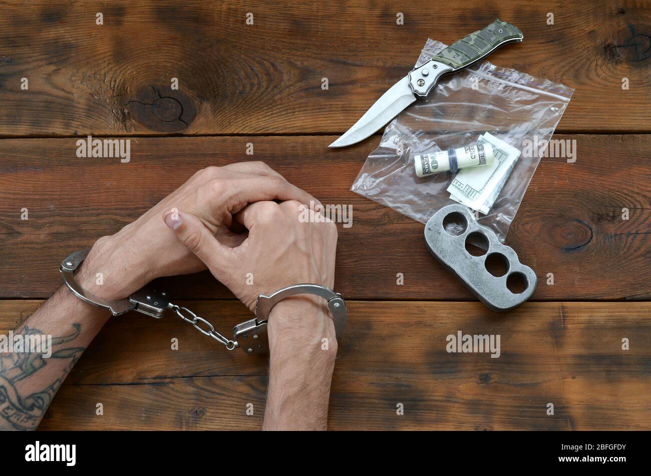 Cuffed hands of tattooed criminal suspect and plastic ziplock packet of  evidence for investigation. Dirty money bills with jackknife and brass  knuckle Stock Photo - Alamy