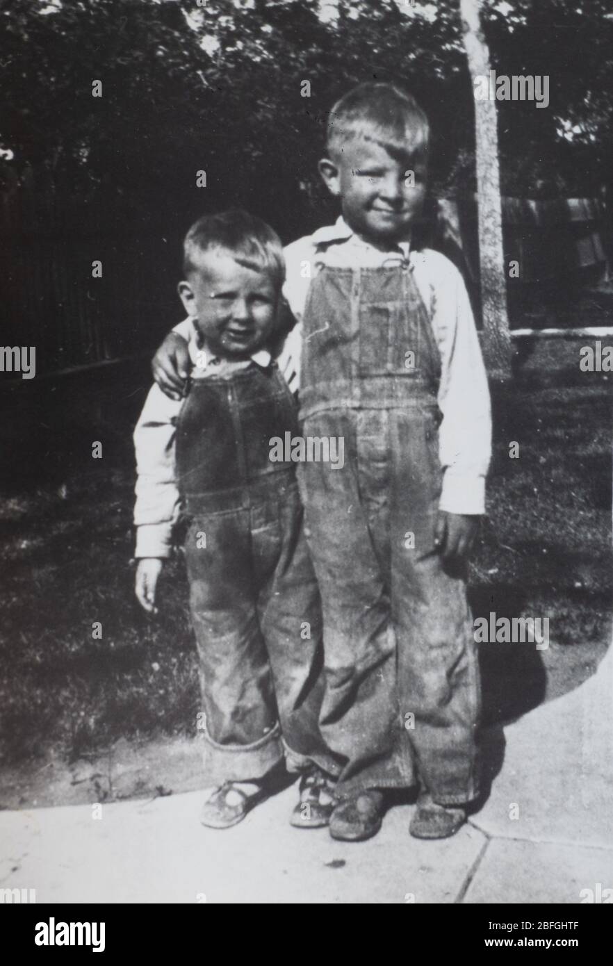 Close up of two brothers wearing denim overalls photographed in the 1930s with the big brother's arm around the little brother's shoulders. Stock Photo