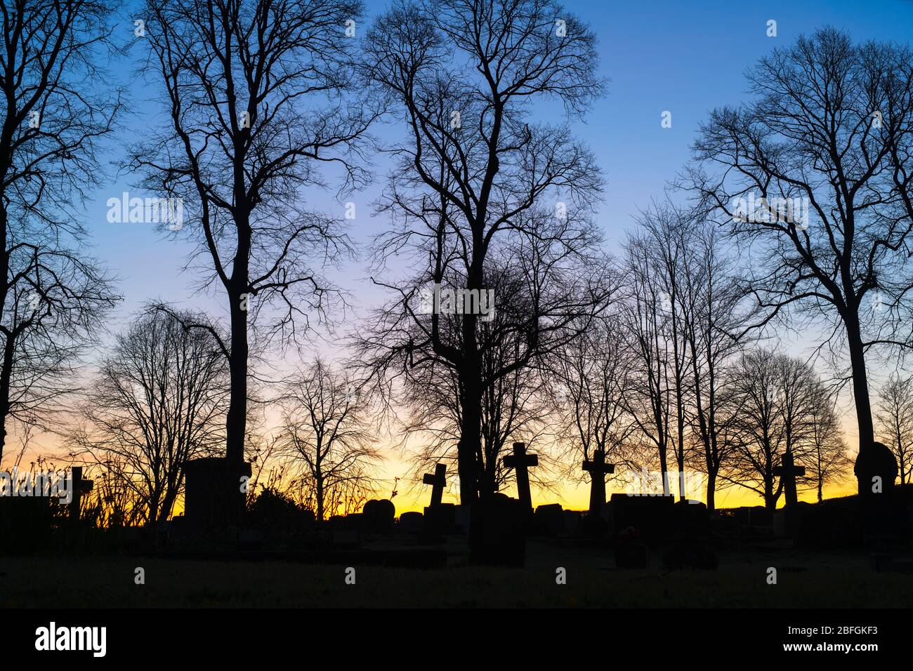 Silhouette of cross headstones and trees in a cemetery at dawn. Kings Sutton, Northamptonshire, England. Silhouette Stock Photo