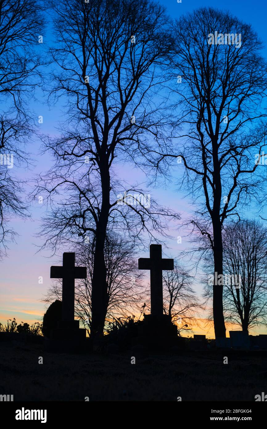 Silhouette of cross headstones and trees in a cemetery at dawn. Kings Sutton, Northamptonshire, England. Silhouette Stock Photo