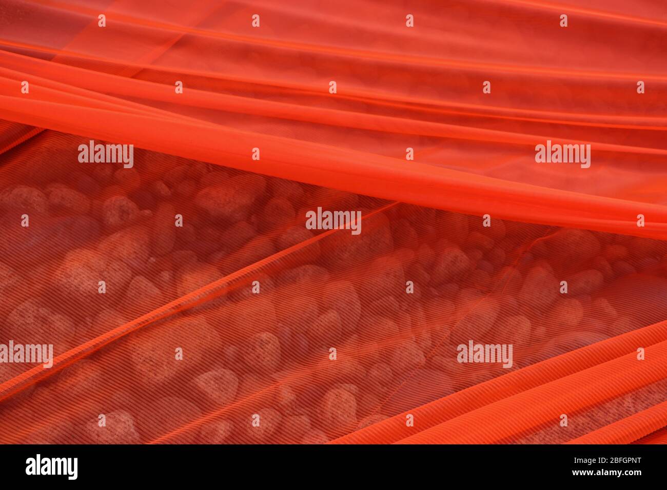 Soft open mesh orange shade cloth stretched over a bed of rocks that can be partially seen through it. Diagonal lines, good for background, copy. Stock Photo