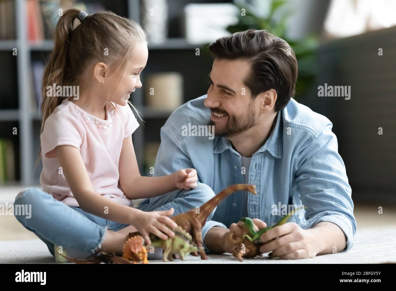 Father and daughter on warm floor playing with dinosaurs toys Stock Photo