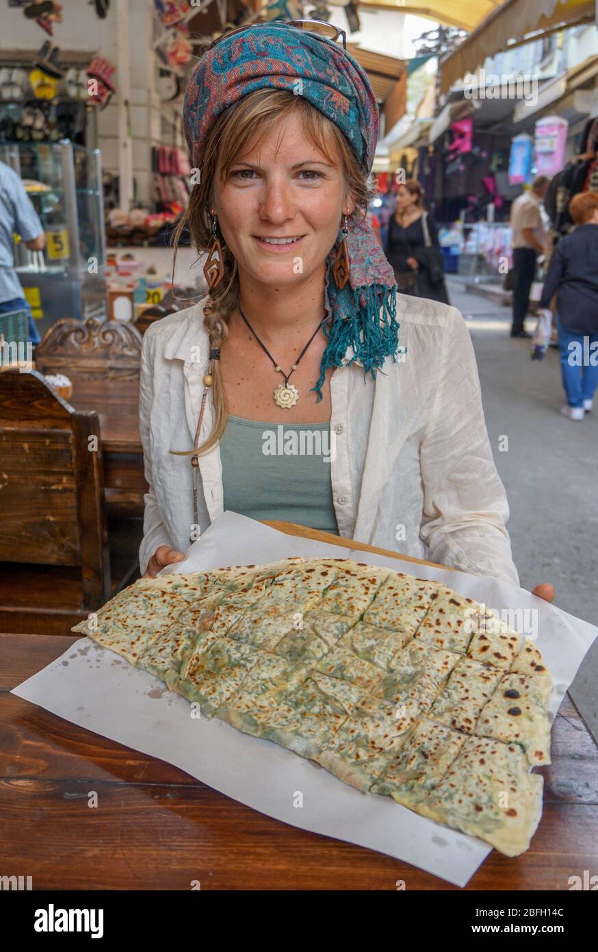 Typical Turkish meal big Gozleme with spinach and mushroom on light wooden cutting board hold by a woman with headscarf in the streets of Istanbul Stock Photo