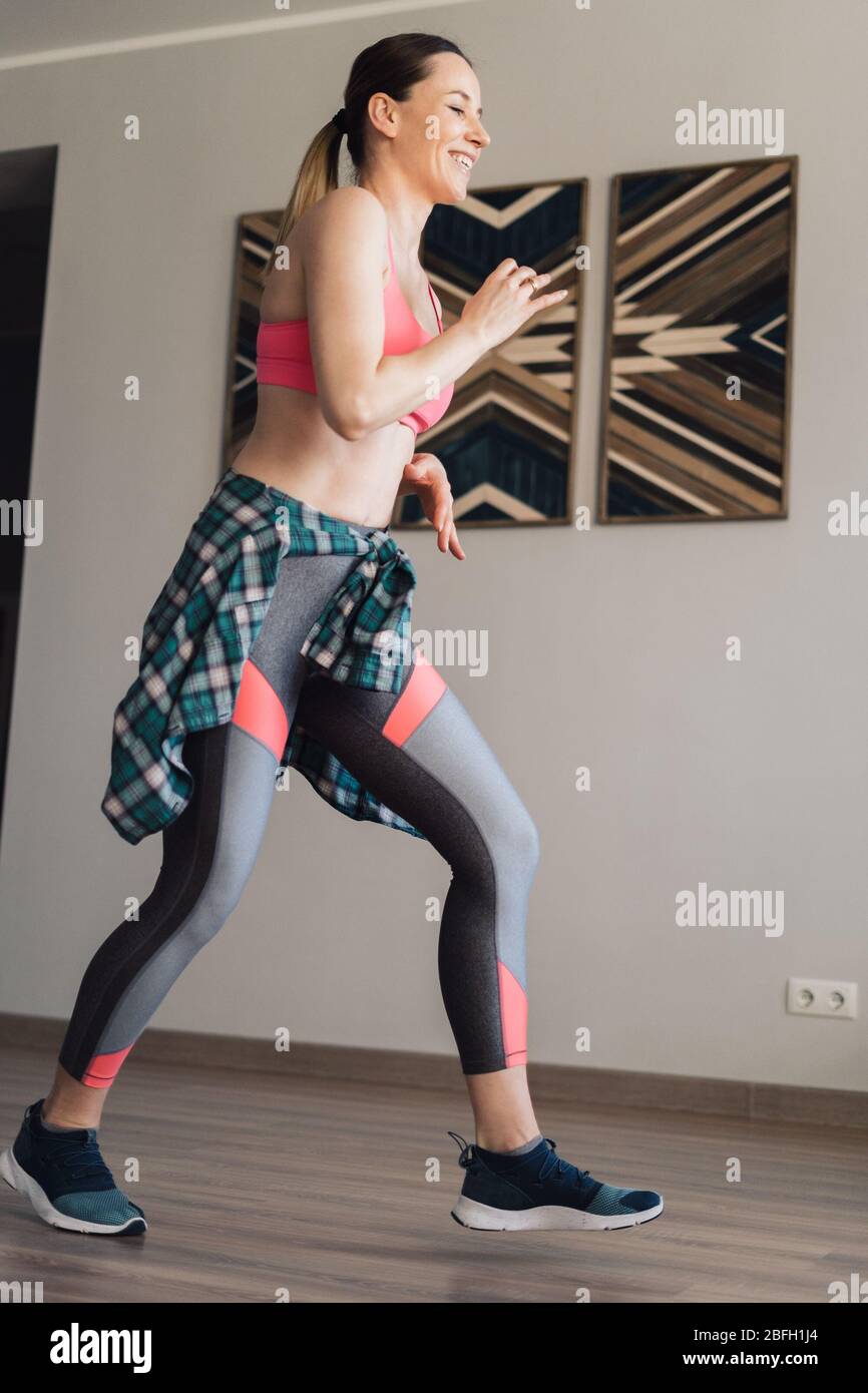 Active young woman in sportswear clothes dancing in living room with