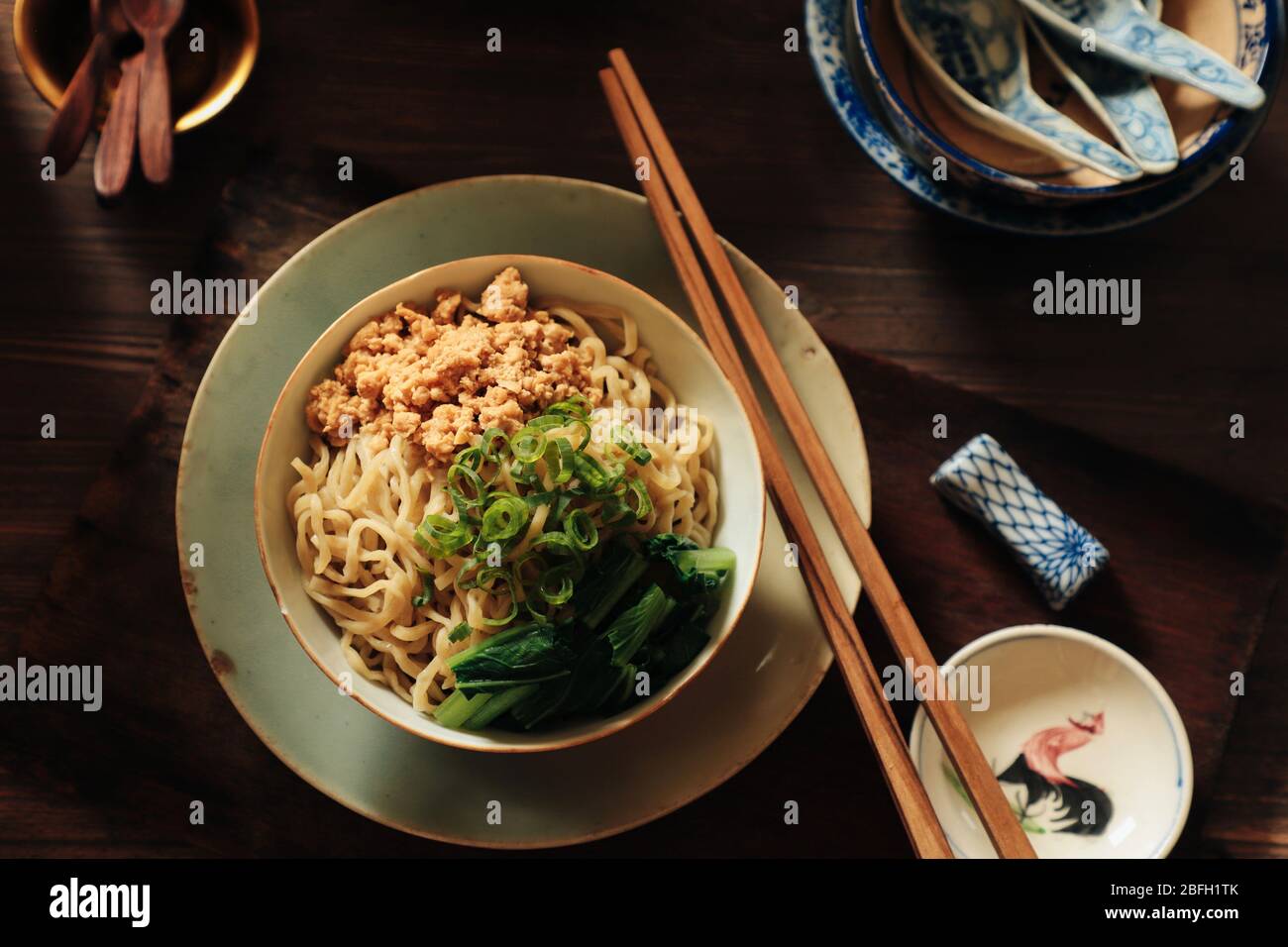 Egg Noodles with Minced Chicken. A Chinese staple food of yellow noodles with soy flavoured minced chicken and choy sum; plated on vintage crockery. Stock Photo