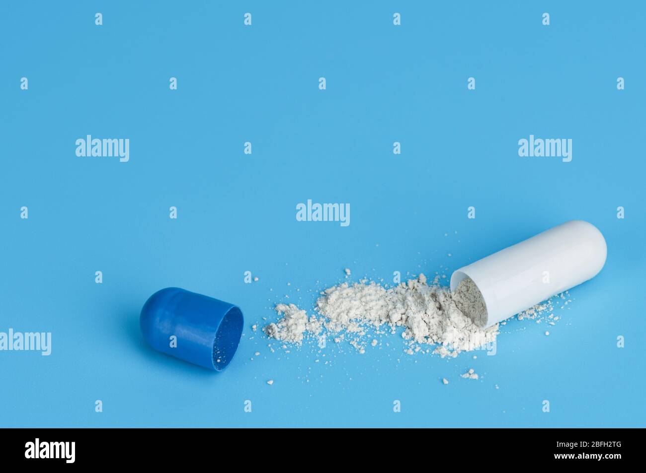 Close up split open medical capsule pill with powder spilled out on a