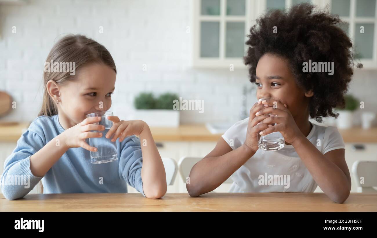Little multiethnic girls drink mineral water at home Stock Photo