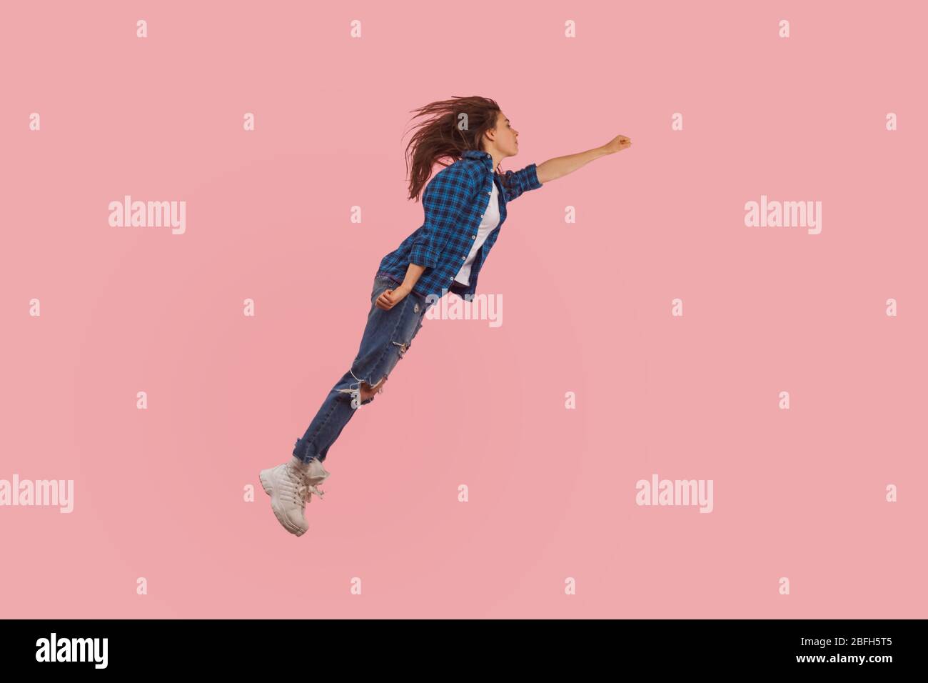 Portrait of girl in casual style outfit flying up in air with raised fist, moving forward to victories, feeling freedom, power and confidence to achie Stock Photo