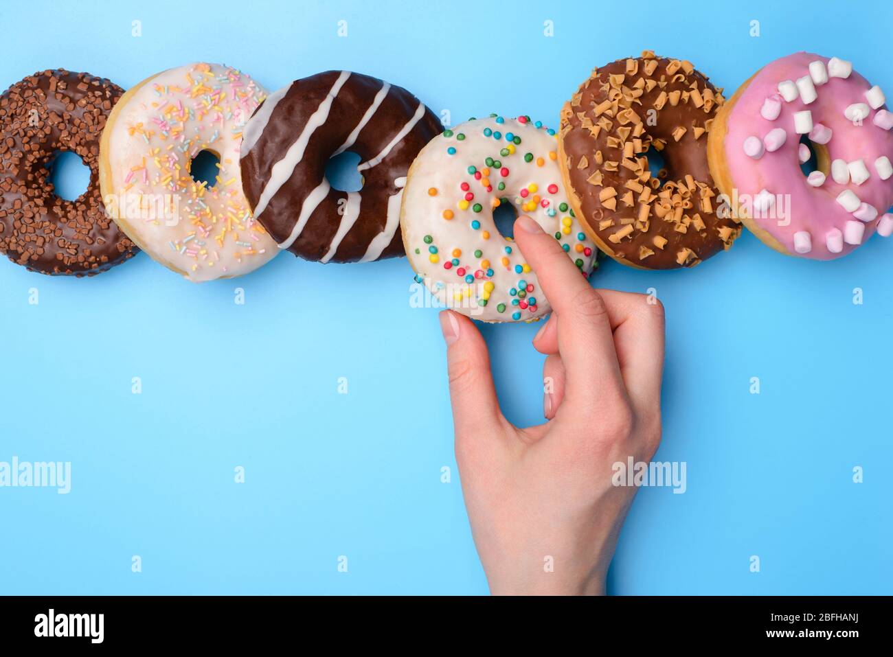 Sweet tooth creative concept. Top above flatlay close up view photo of woman hand taking yummy tasty round donut isolated over blue pastel background Stock Photo