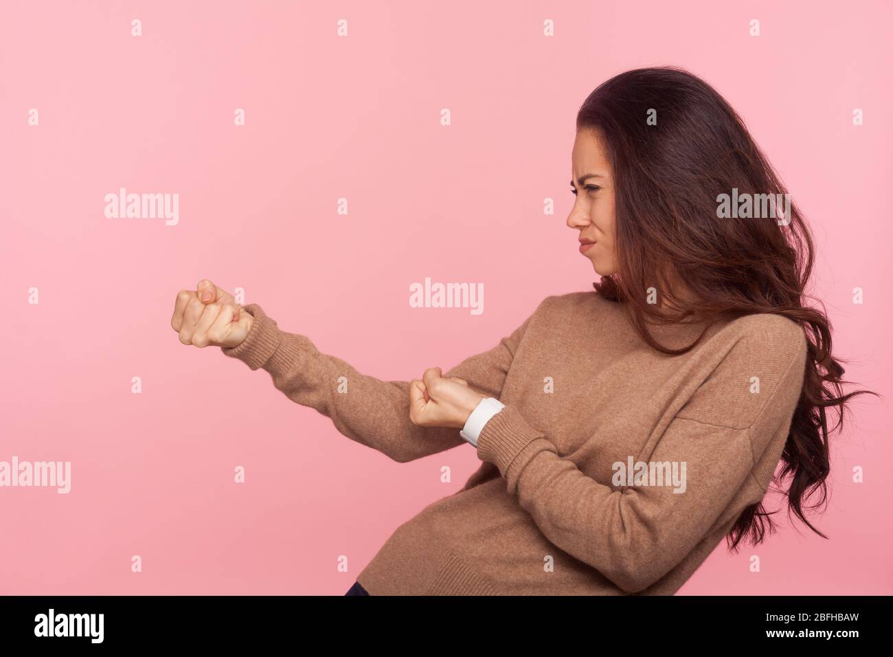 Portrait of diligent purposeful young woman with brunette hair pretending to pull invisible rope, holding something heavy with expression of great eff Stock Photo