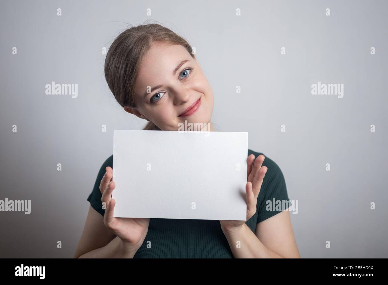 Smiling young Caucasian woman girl holding blank white paper sheet with copy space Stock Photo