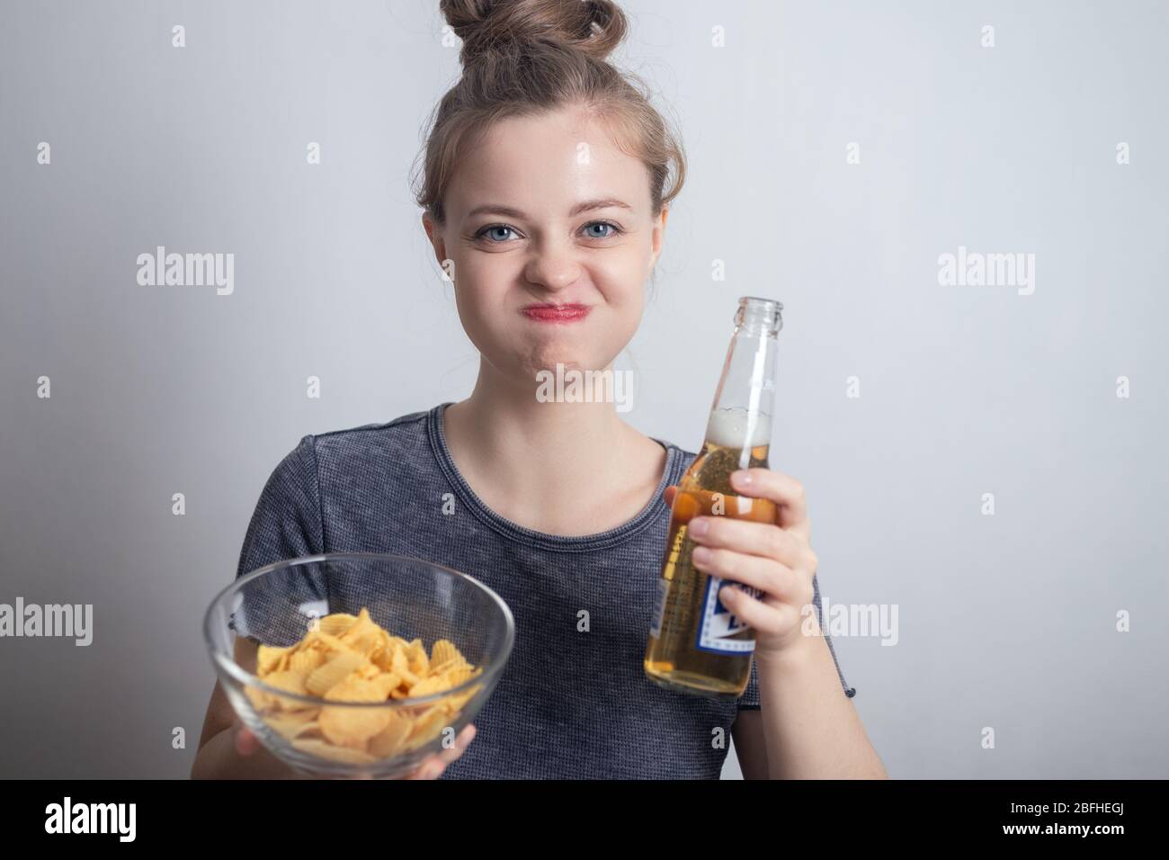 Smiling young caucasian woman girl drinking bottle of beer and holding potato chips crisps Stock Photo