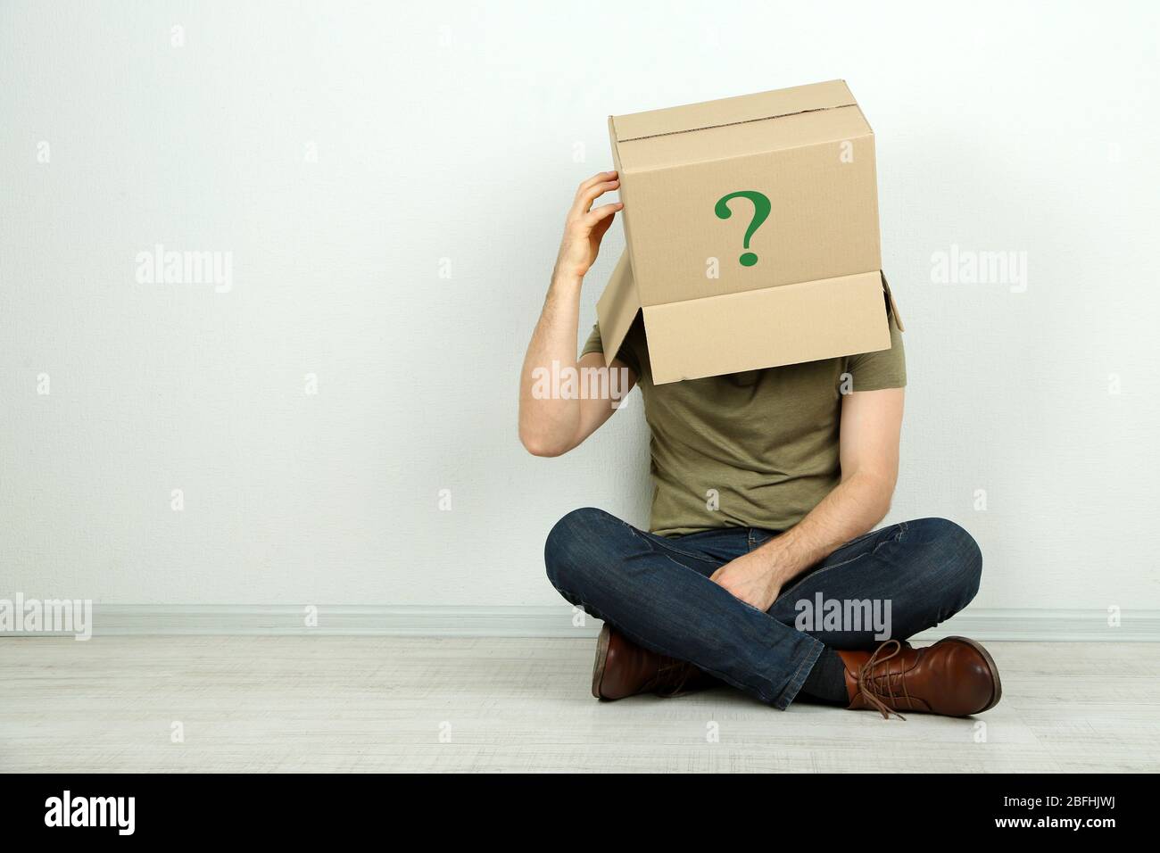 Man with cardboard box on his head sitting on floor near wall Stock ...
