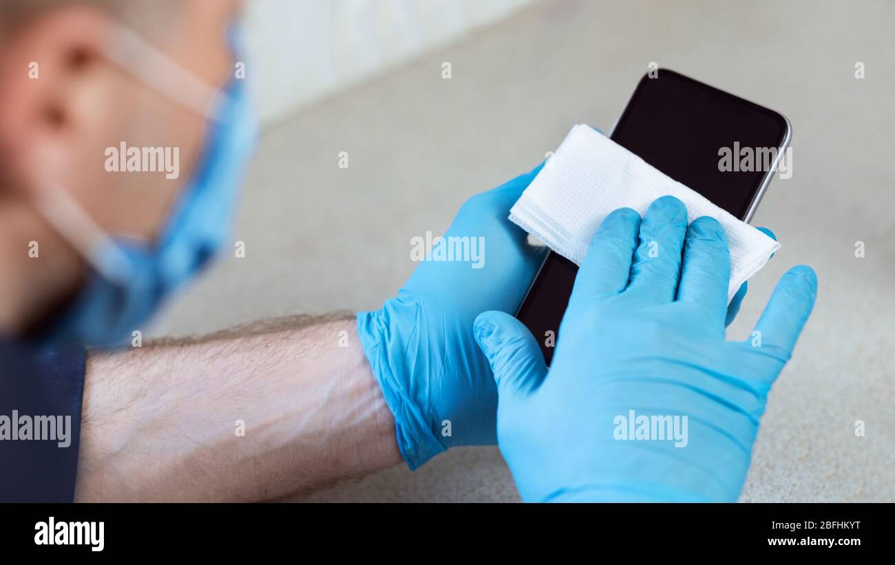 Man Sterilizing Mobile Phone At Home During Coronavirus Pandemic, Cropped Stock Photo