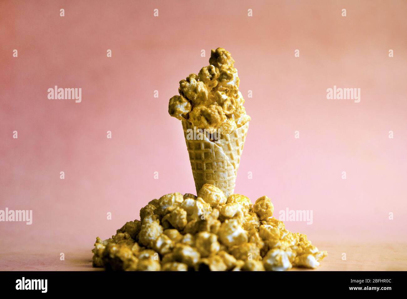 Caramel Popcorn in ice cream cone on pink colorful background. caramel Popcorn on a cone cornucopia. Splitted popcorn on bright hipster background Stock Photo