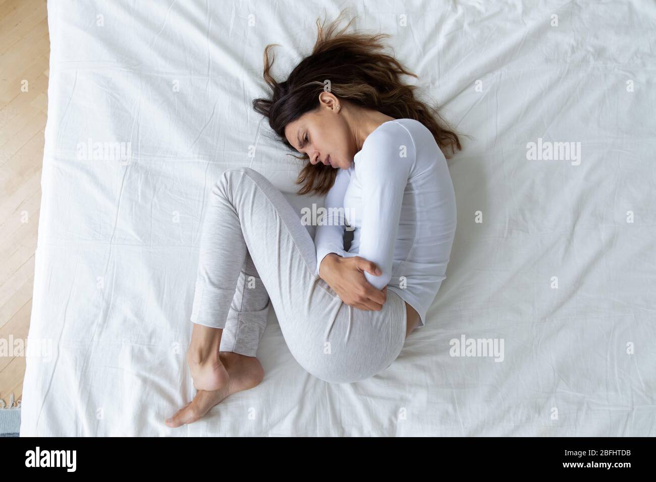 Top view stressed unhappy young woman lying in fetal position Stock Photo