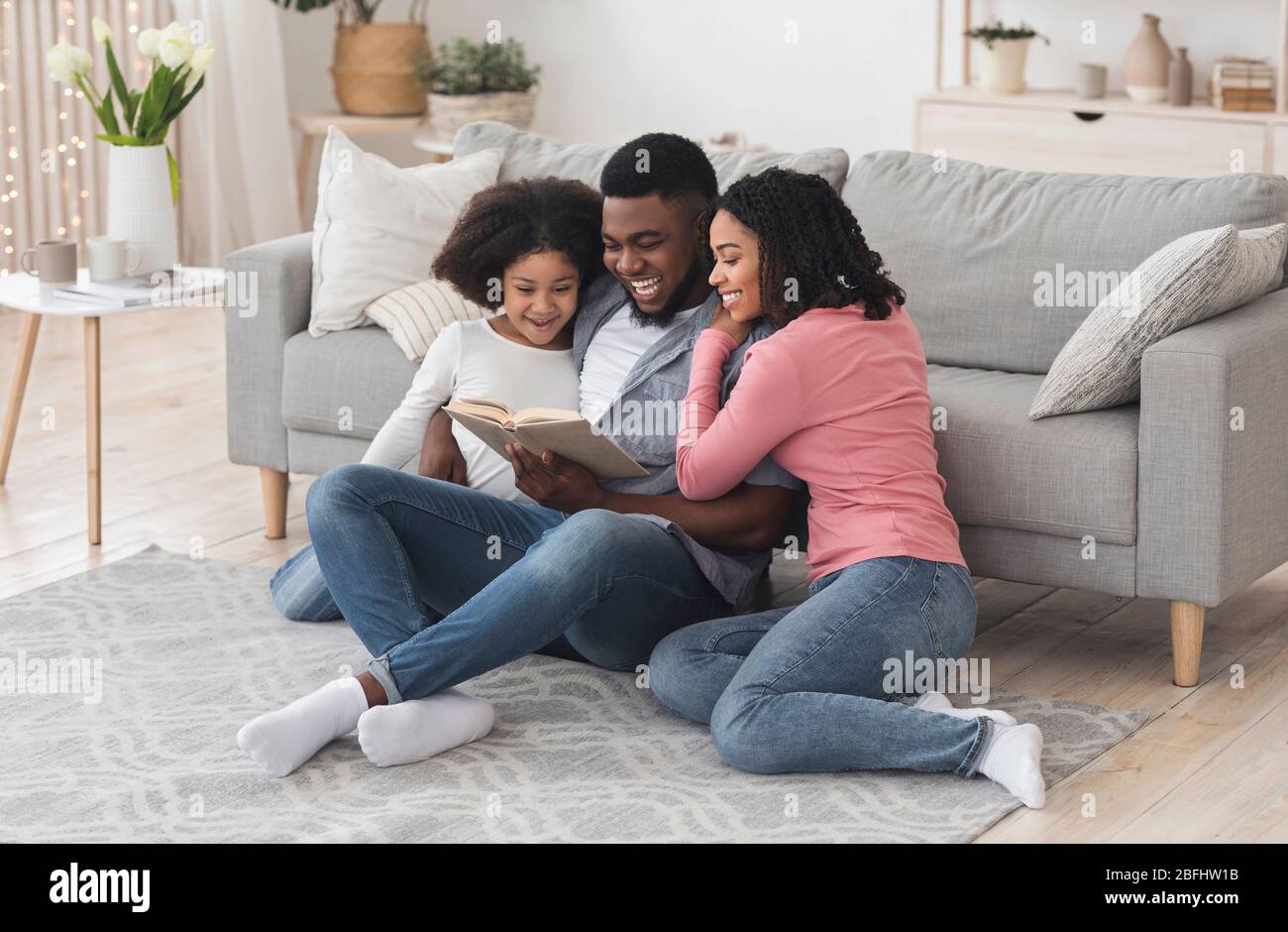 Happy black family reading book together, staying at home during quarantine Stock Photo