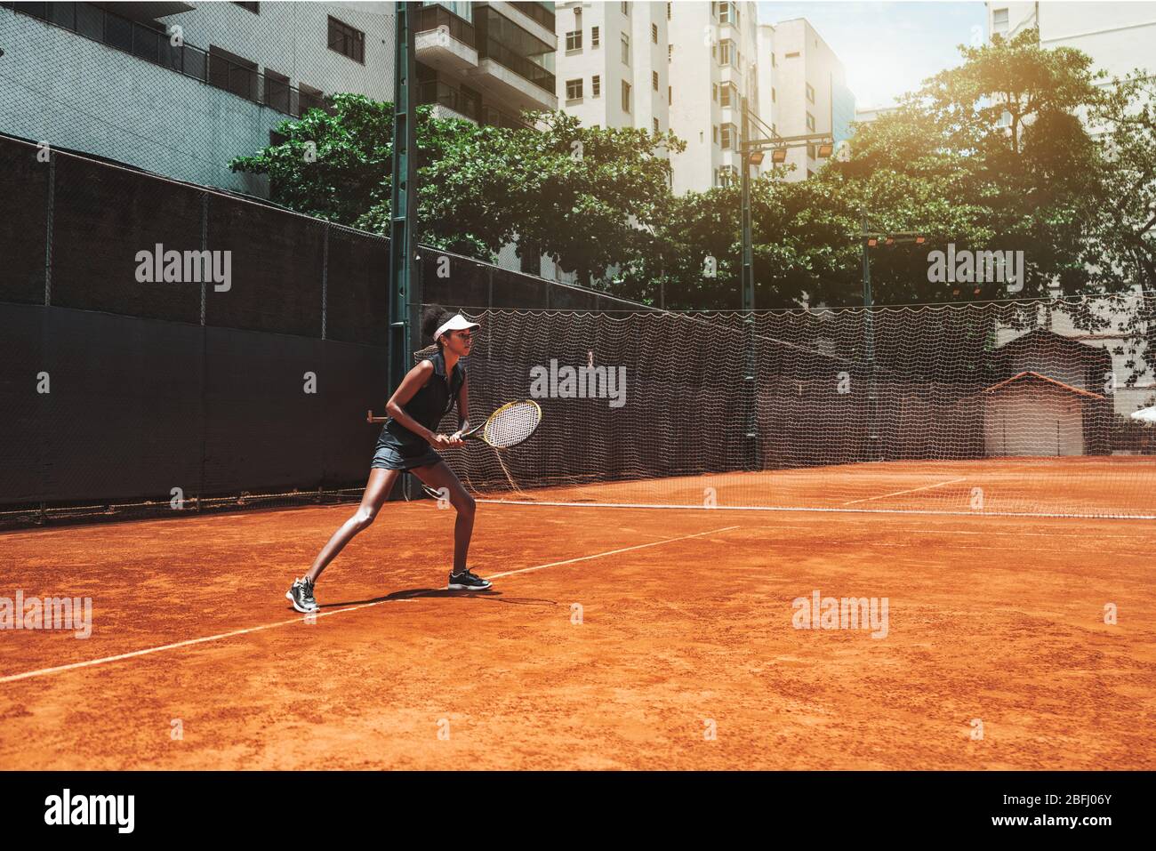 A young slim African-American female plays tennis outdoors in the training court; beautiful biracial sports girl in sports stance ready to deflect ten Stock Photo