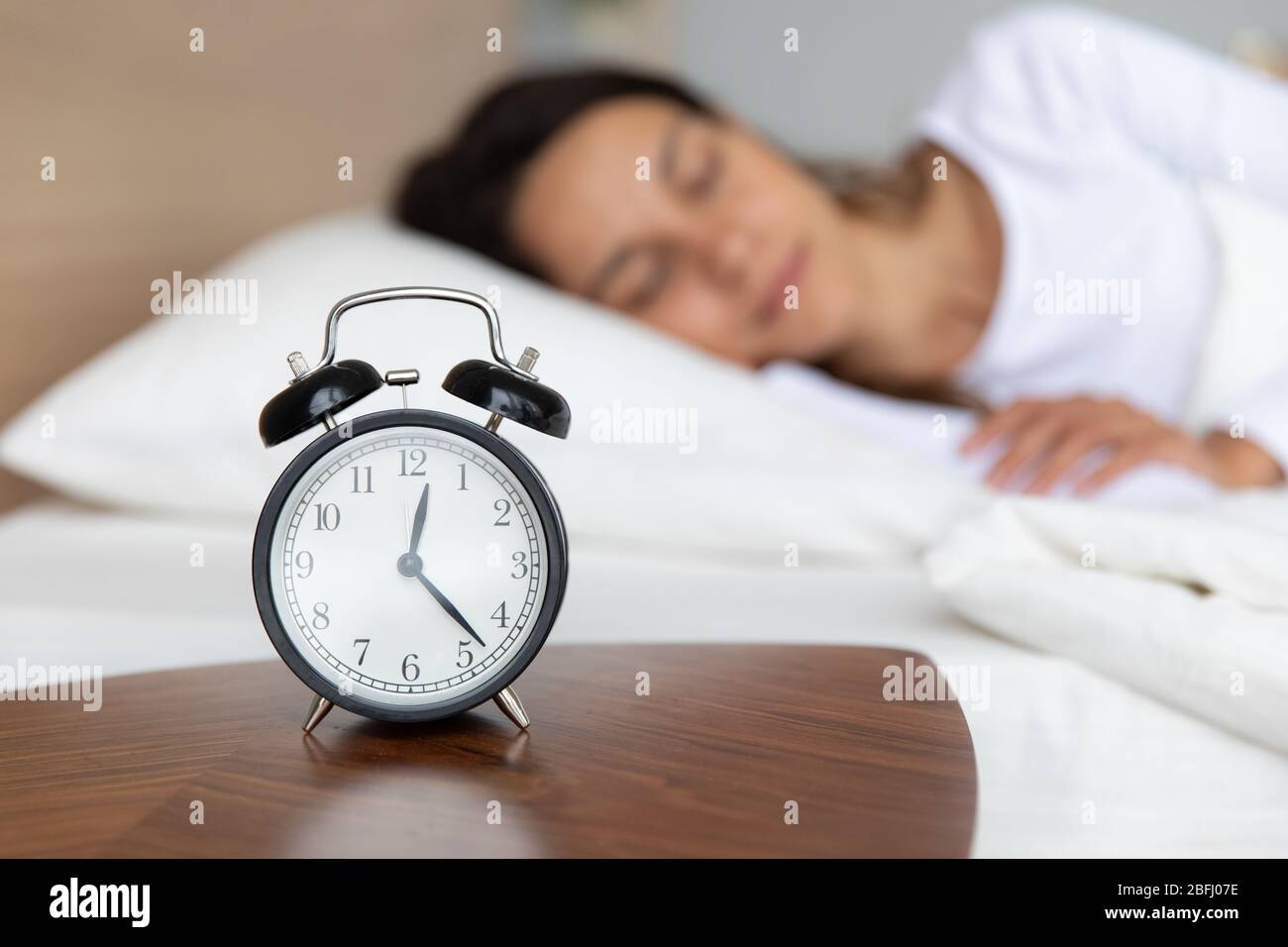 Close up alarm clock on bedside table, peaceful woman sleeping Stock Photo