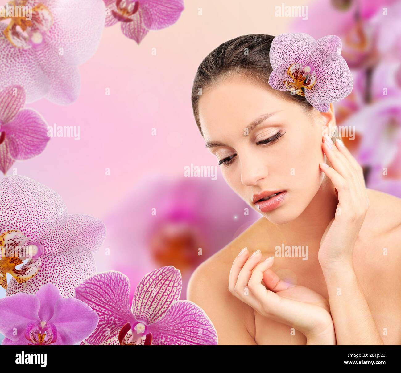 Beautiful young woman with orchid flower in hair on pink orchid flowers ...