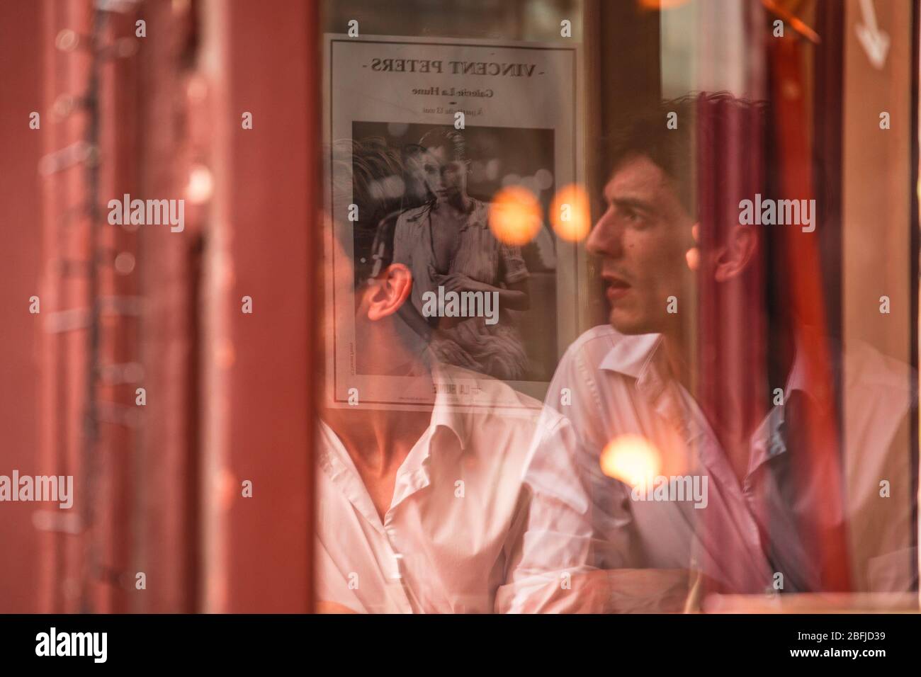 Profile reflected portrait of a man sitting by a window in a cafe with a poster of the model Laetita Casta behind, Paris Stock Photo