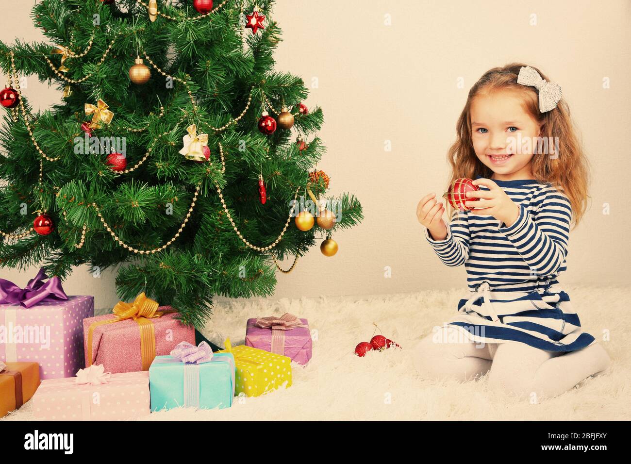 Little girl decorating Christmas tree with baubles in room Stock Photo ...