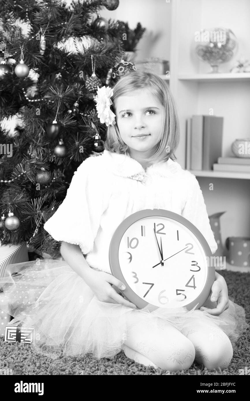 Little girl holding clock near Christmas tree in room Stock Photo