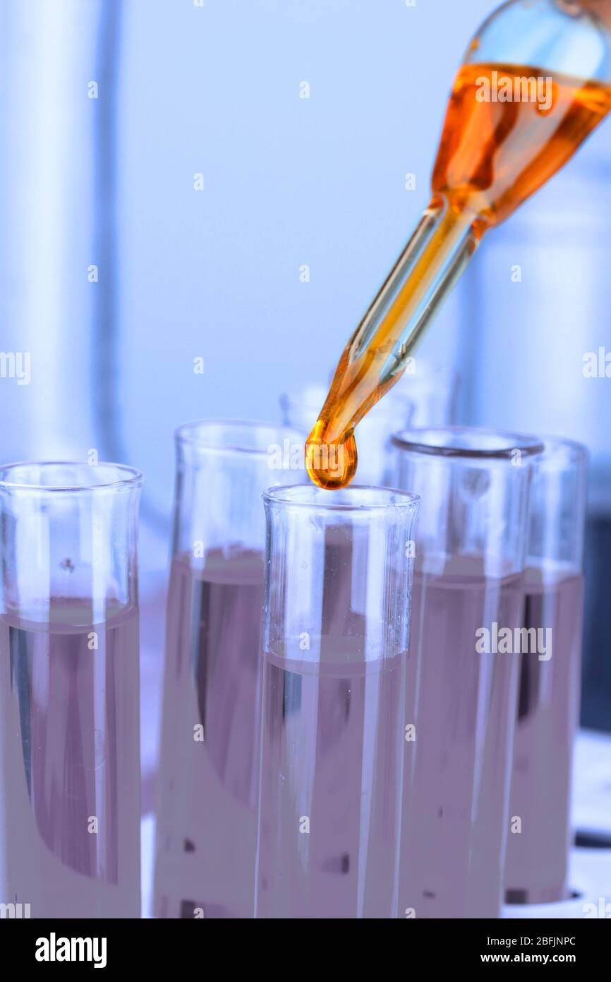 Laboratory pipette with drop of color liquid over glass test tubes ...
