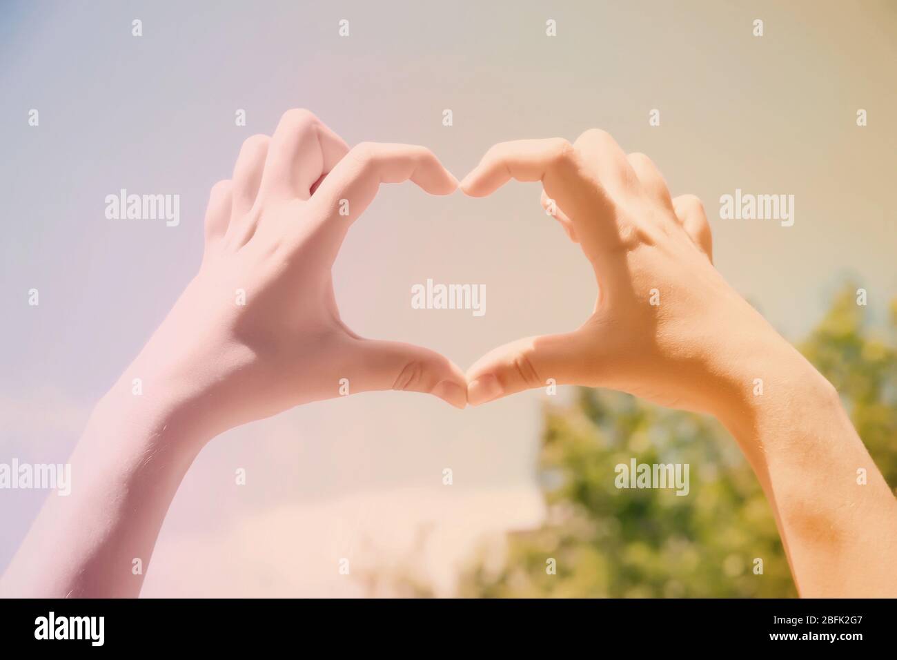 Young woman holding hands in heart shape framing on blue sky background ...