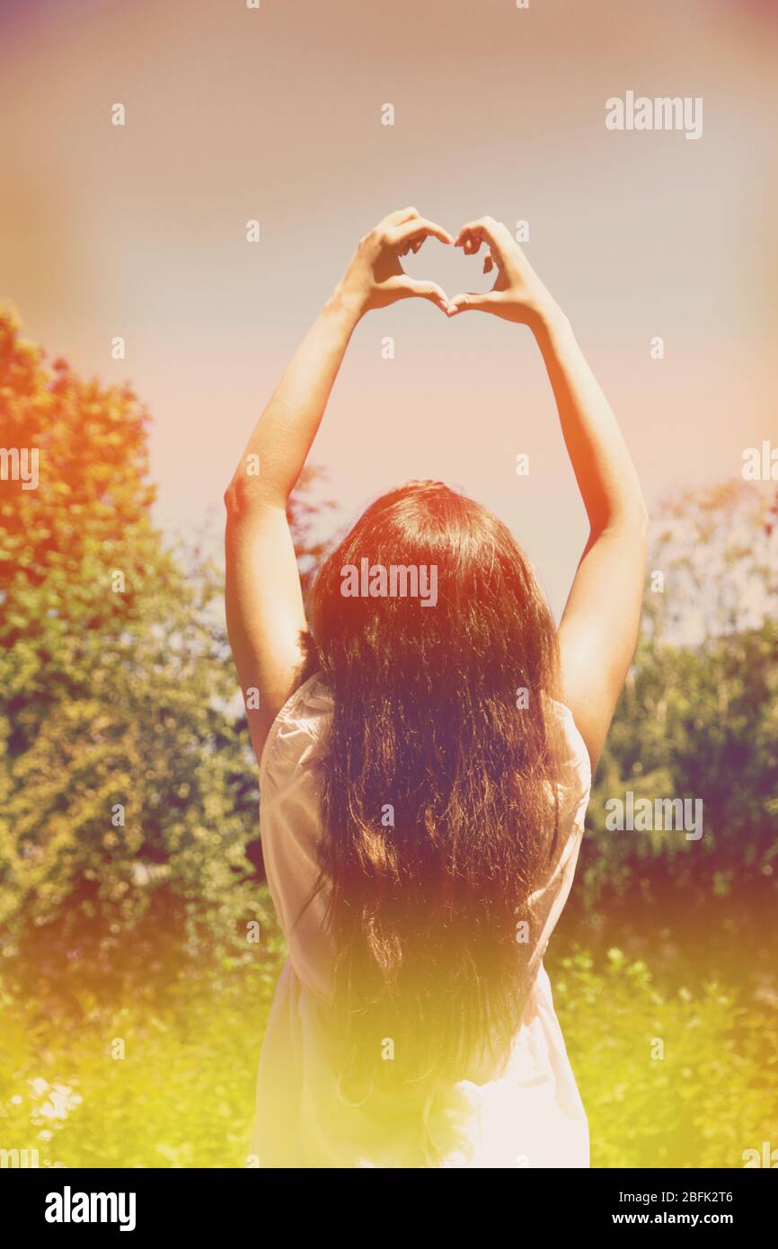 Young woman holding hands in heart shape framing on sky background ...
