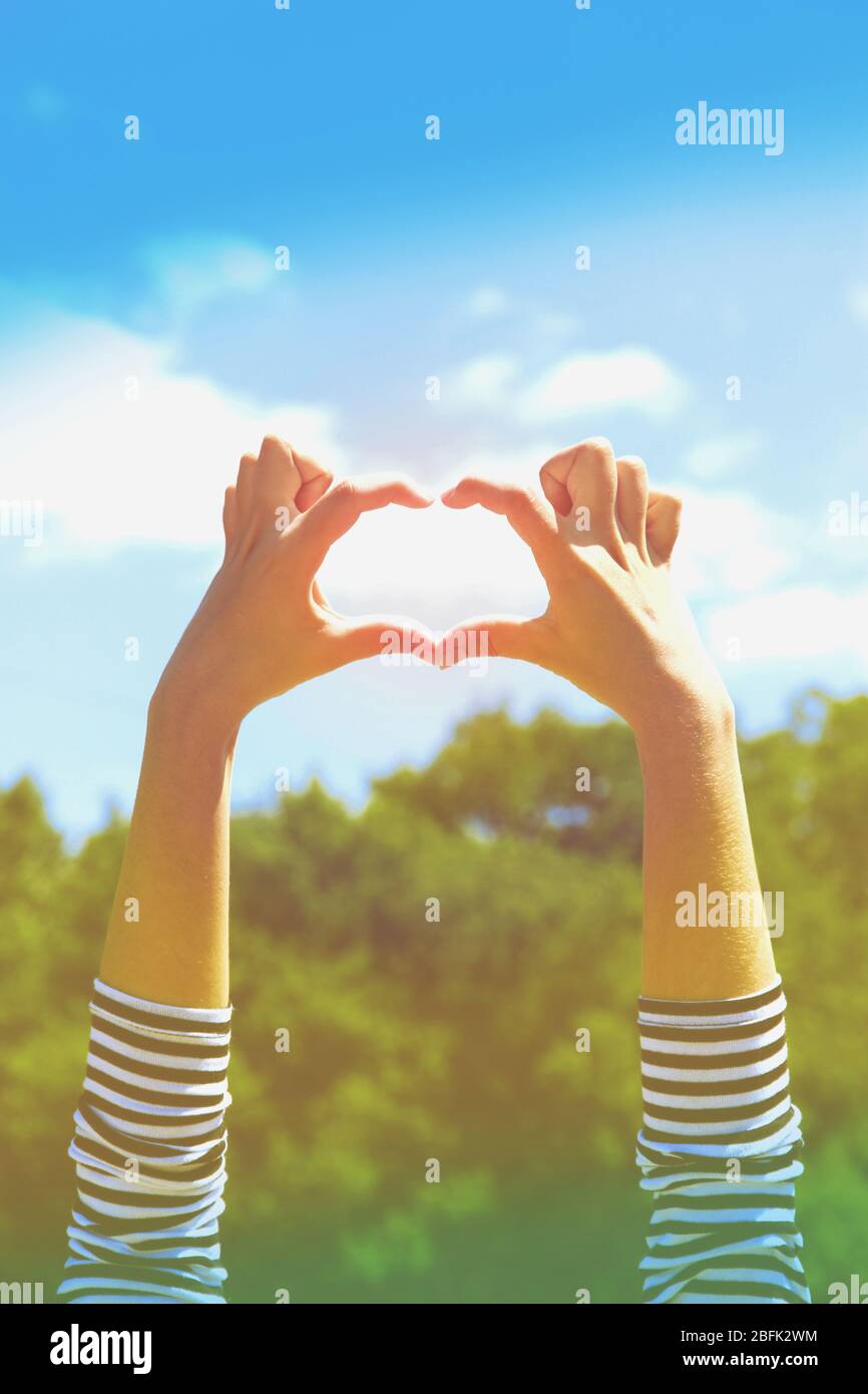 Young woman's hands making heart shape frame on blue sky background ...