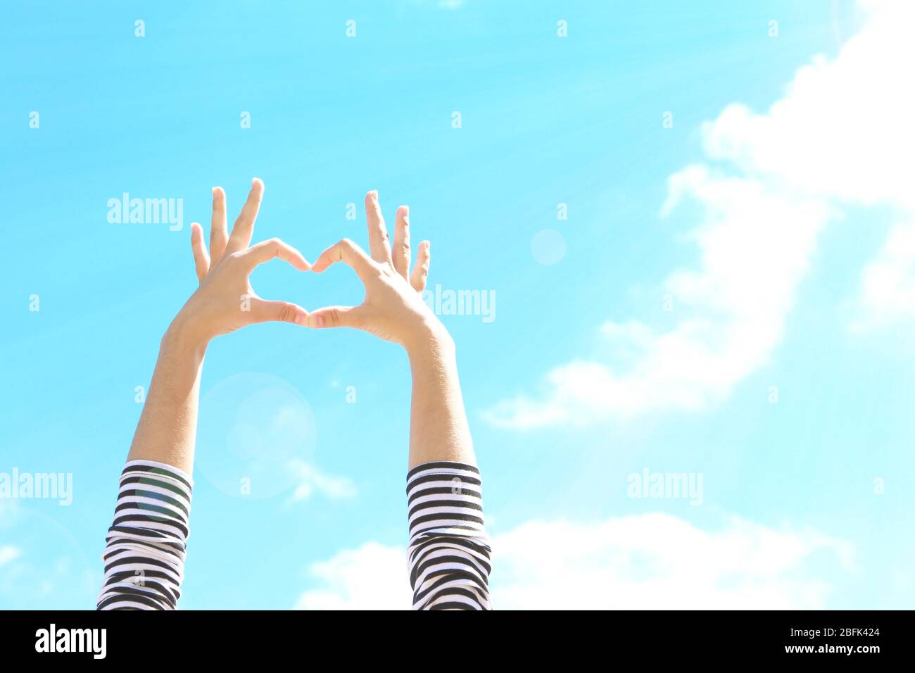 Young woman's hands making heart shape frame on blue sky background ...