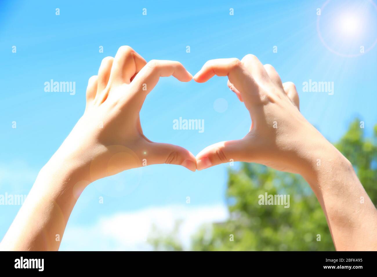Young woman's hands making heart shape frame on blue sky background ...
