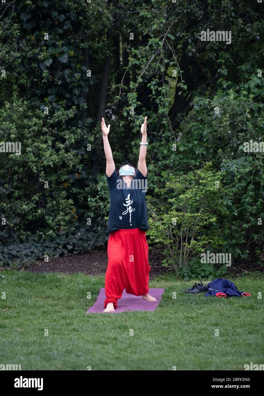 Woman wearing a face mask and exercising yoga in Kensington Park, London during lockdown.  Health secretary, Matt Hancock, said the public must resist the urge to flout physical distancing rules to prevent tighter lockdown rules being enforced. Stock Photo