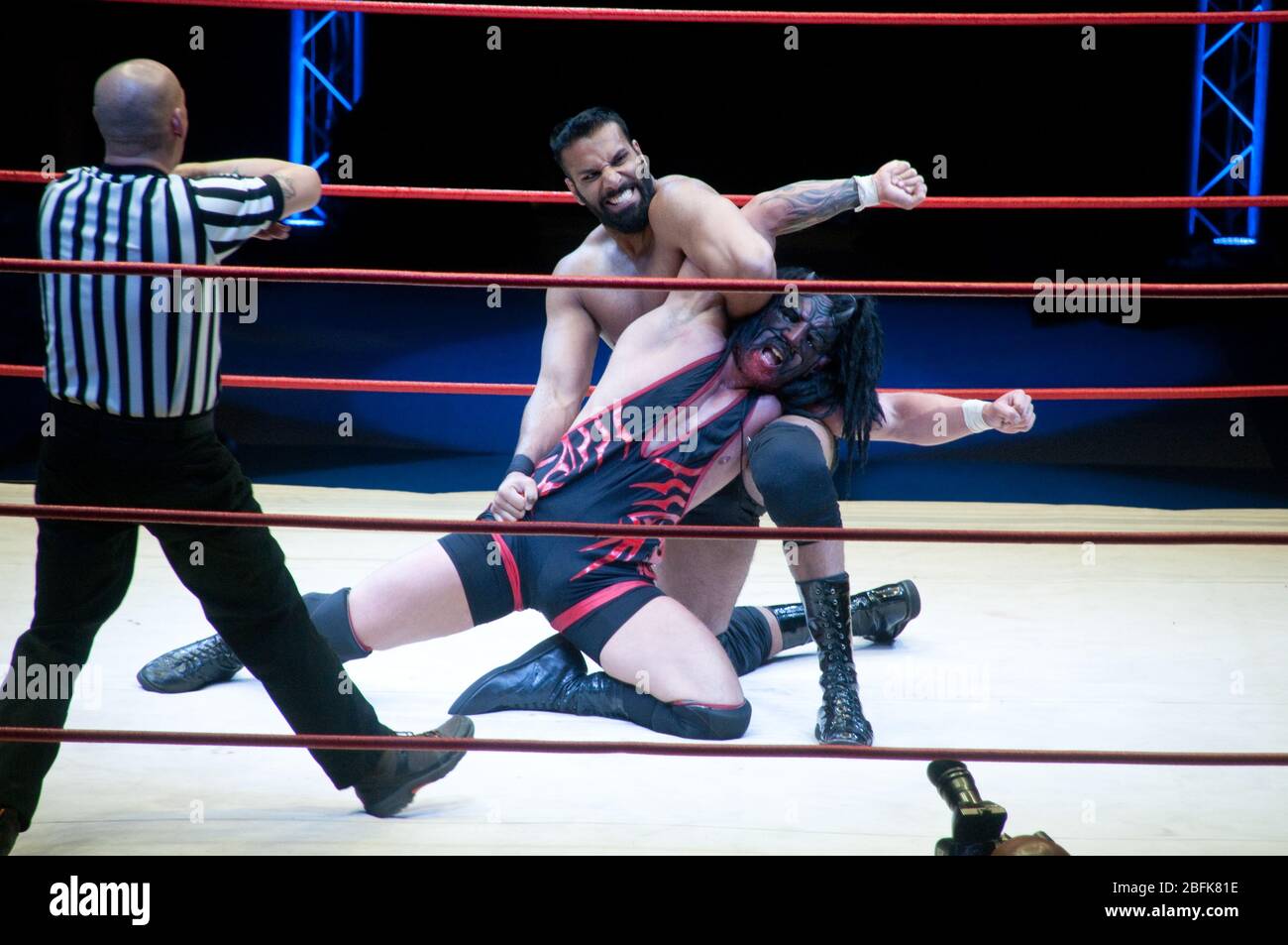 Two male professional wrestlers fighting in the ring beside a referee, at a live outdoor wrestling match in the city of Doha, in Qatar. Stock Photo