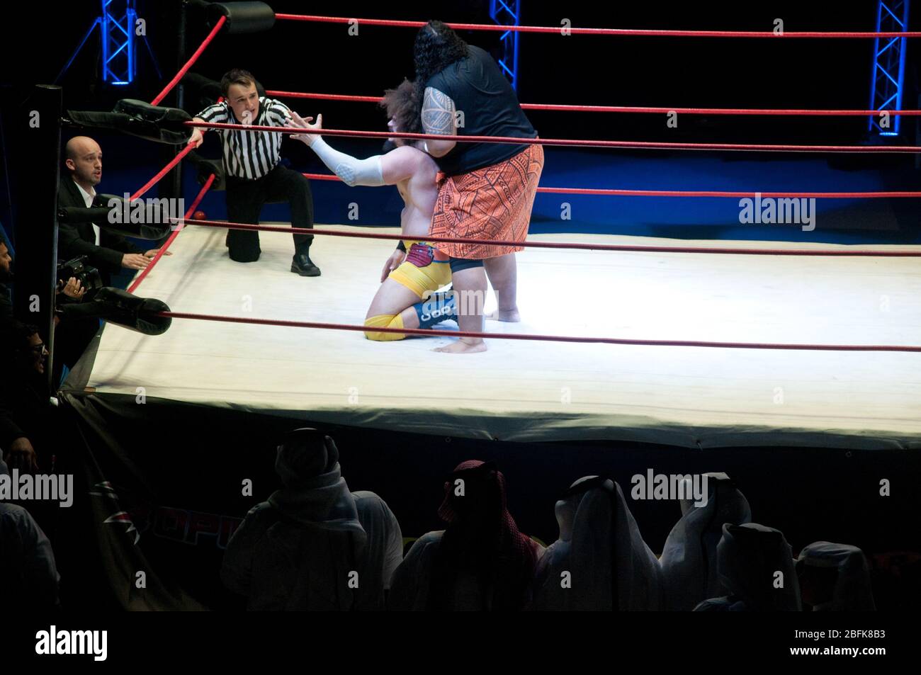 Two male professional wrestlers fighting in the ring beside a referee and a manager, at a live outdoor wrestling match in the city of Doha, in Qatar. Stock Photo