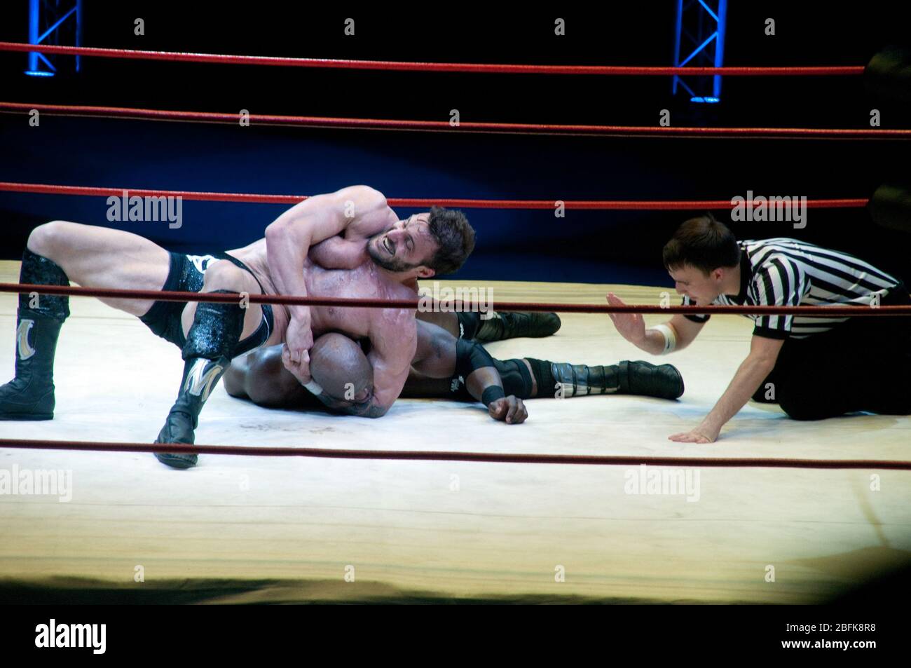 Two male professional wrestlers fighting in the ring beside a referee, at a live outdoor wrestling match in the city of Doha, in Qatar. Stock Photo