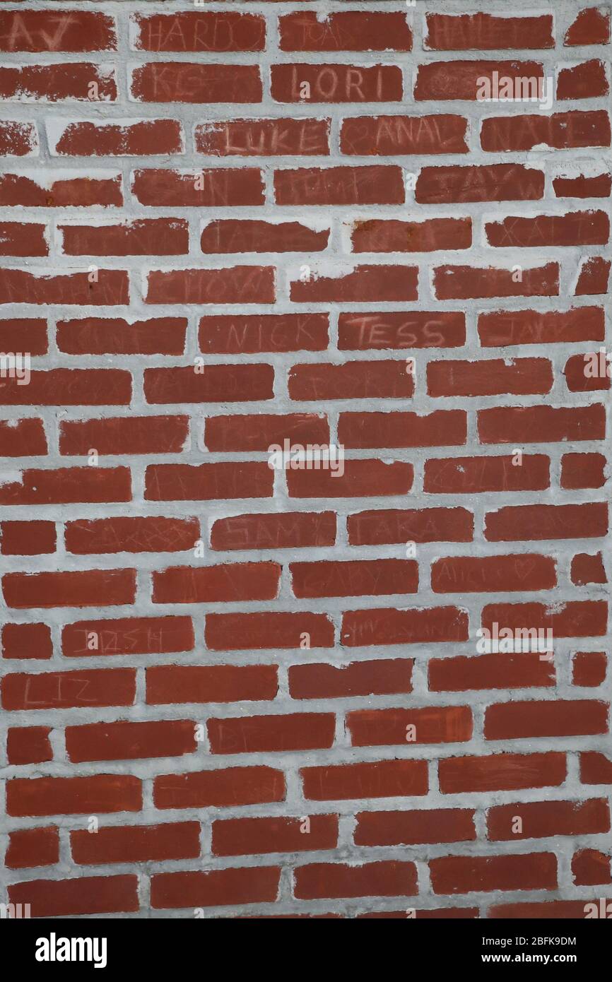 red brick wall with white cement lines and names etched into the bricks Stock Photo