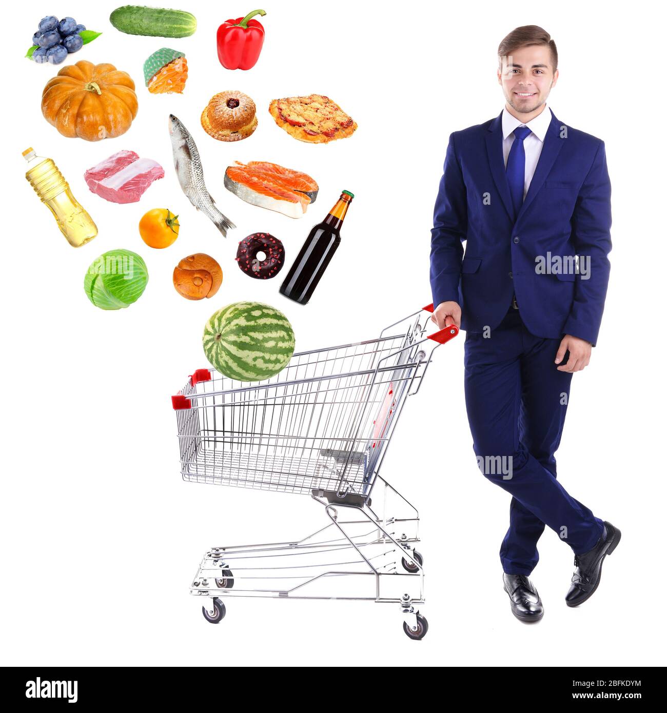Young man holding shopping cart with different food, isolated on white