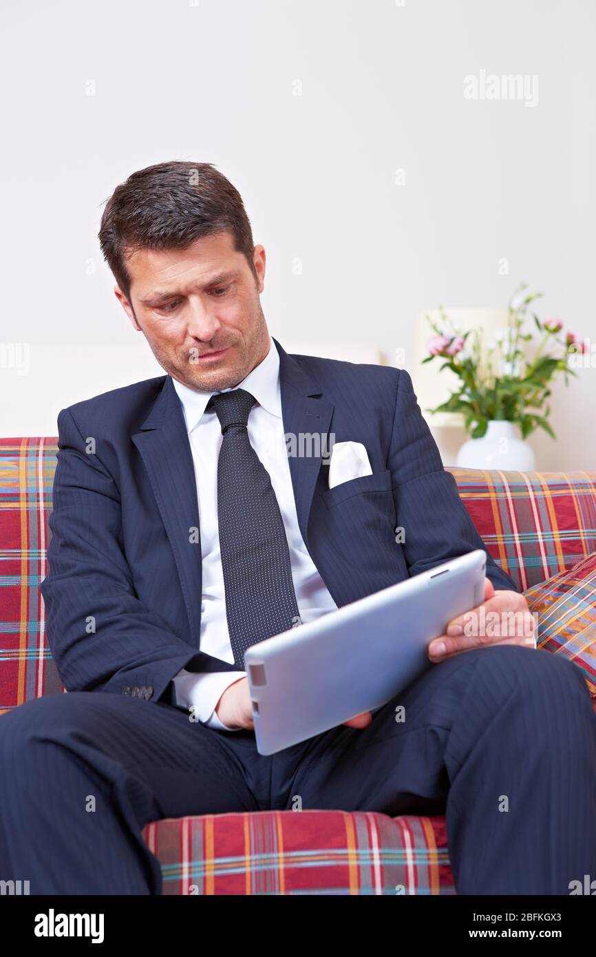 Manager in suit works on tablet computer on sofa Stock Photo