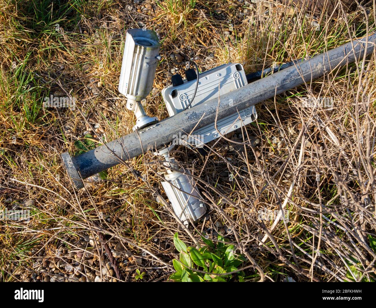 A broken security camera mounted on a pole laying flat on grass Stock Photo