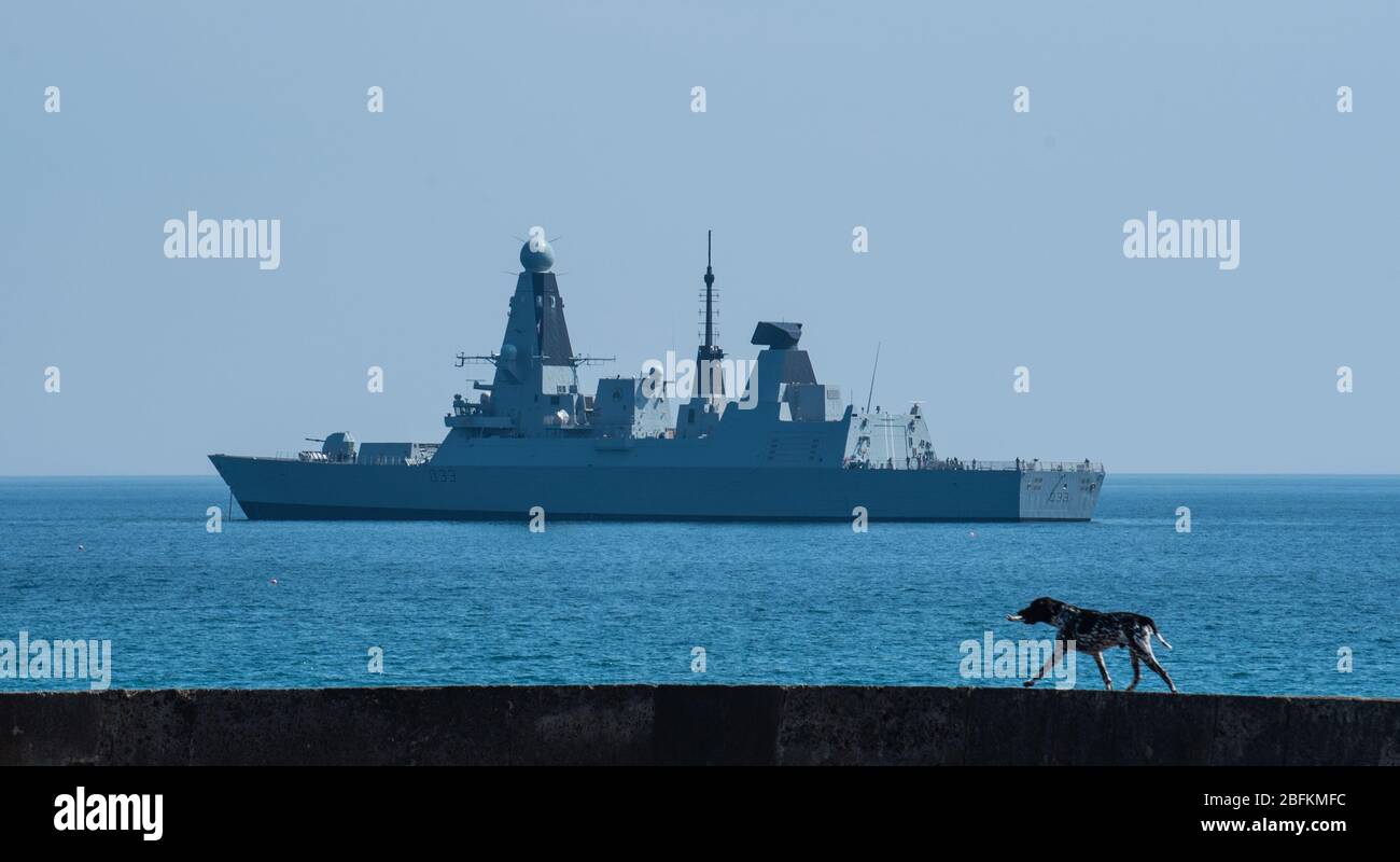 Lyme Regis, Dorset, UK. 19th Apr, 2020. UK Weather: Royal Navy Warship HMS Dauntless anchored at Lyme Regis on a warm and sunny afternoon during the coronavirus lockdown. A dog walks along the Cobb wall with HMS Dauntless in the background. Credit: Celia McMahon/Alamy Live News Stock Photo