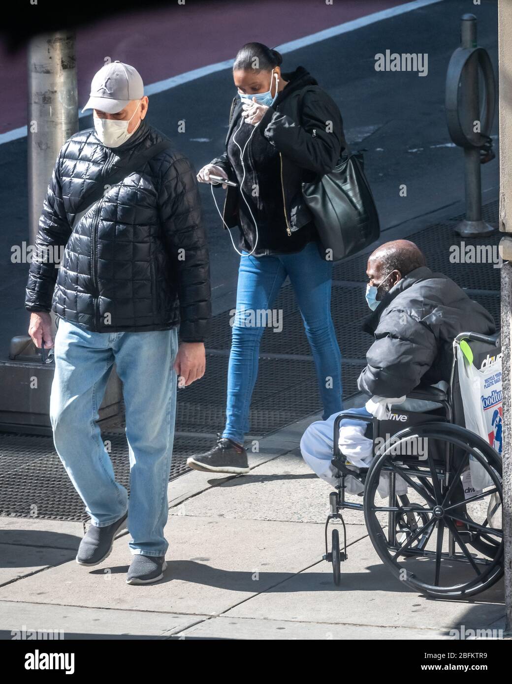 New York, USA. 19th Apr, 2020. Wearing face masks, people walk past a homeless beggar in New York City. The government stated that Newyorkers should cover their faces when they go outside and cannot mantain social distancing, to prevent coronavirus spread. Credit: Enrique Shore/Alamy Live News Stock Photo