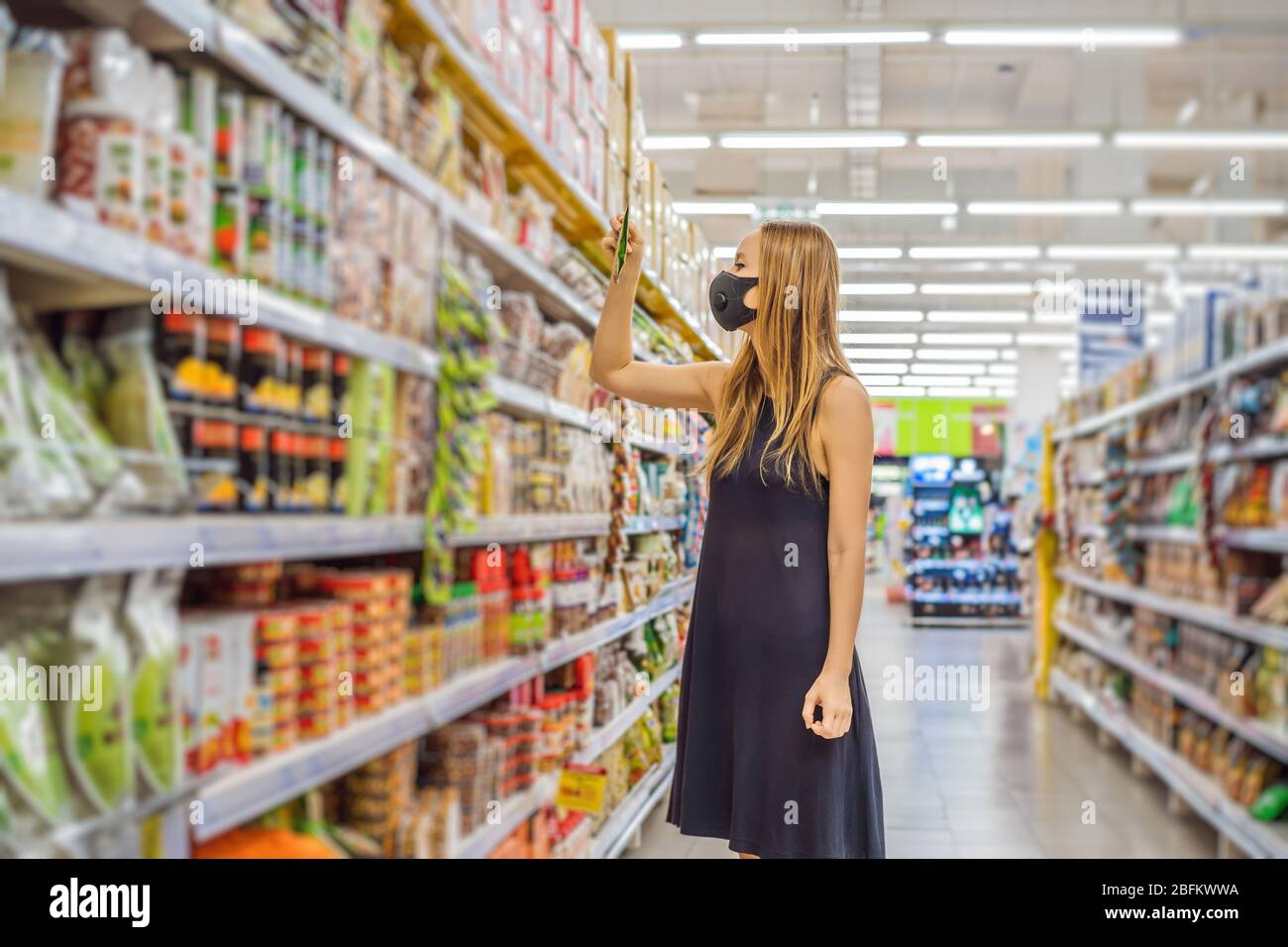 Alarmed female wears medical mask against coronavirus while grocery shopping in supermarket or store- health, safety and pandemic concept - young Stock Photo