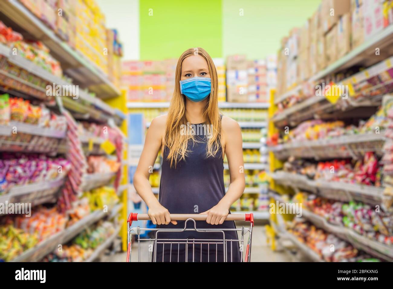 Alarmed female wears medical mask against coronavirus while grocery shopping in supermarket or store- health, safety and pandemic concept - young Stock Photo