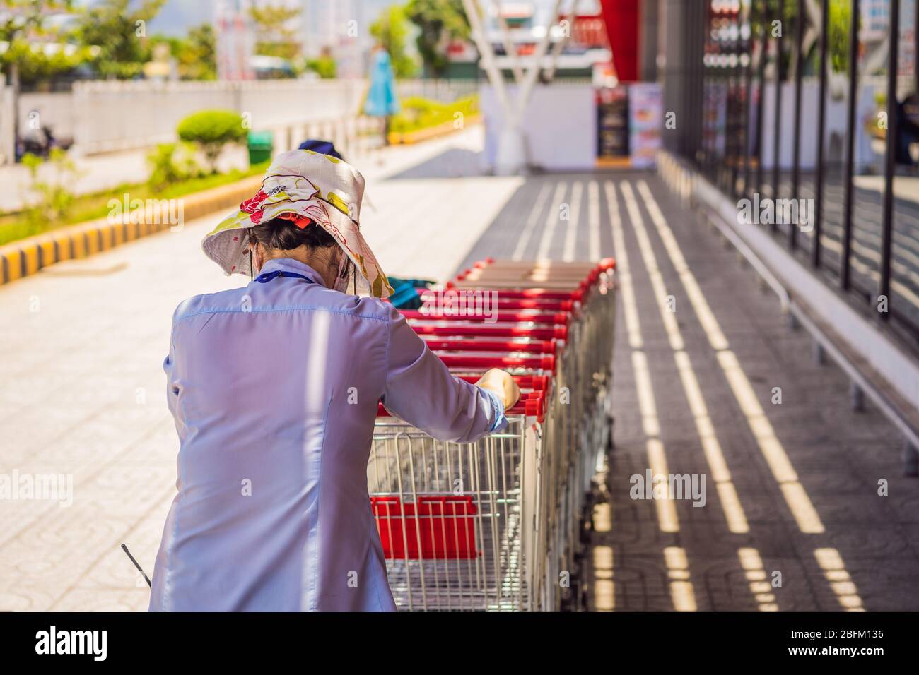 Female employee collects shopping trolleys outside a branch of supermarket chain Stock Photo